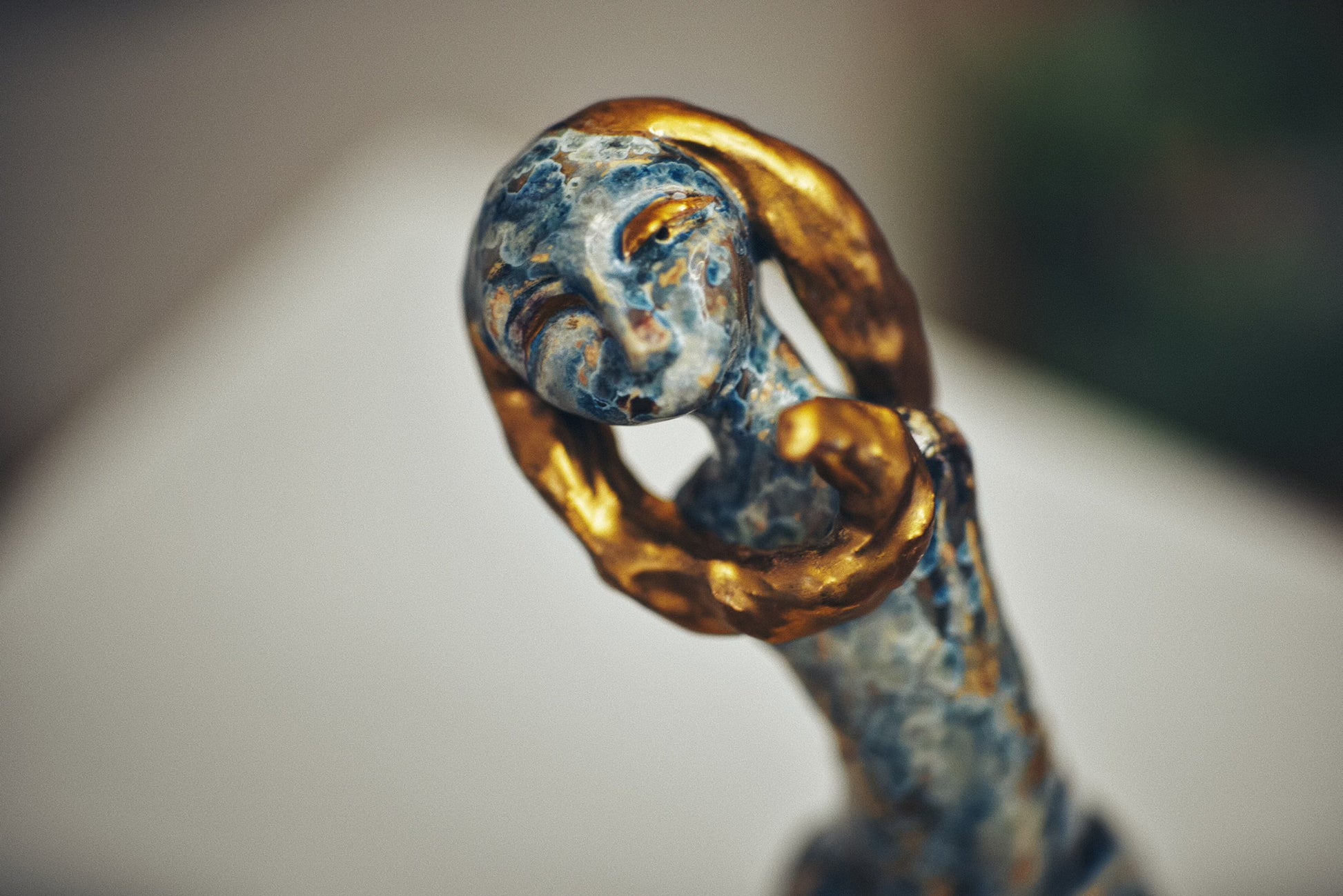 Close-up of a decorative ceramic object with gold and blue patina on a blurred background