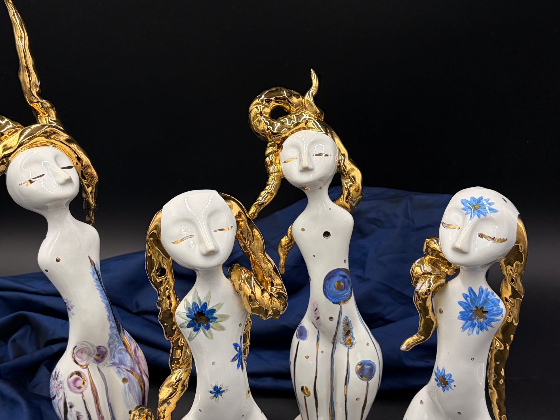 Decorative figurines of women with gold hairpieces and blue floral designs on a dark background