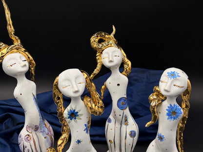 Decorative figurines of women with gold hairpieces and blue floral designs on a dark background