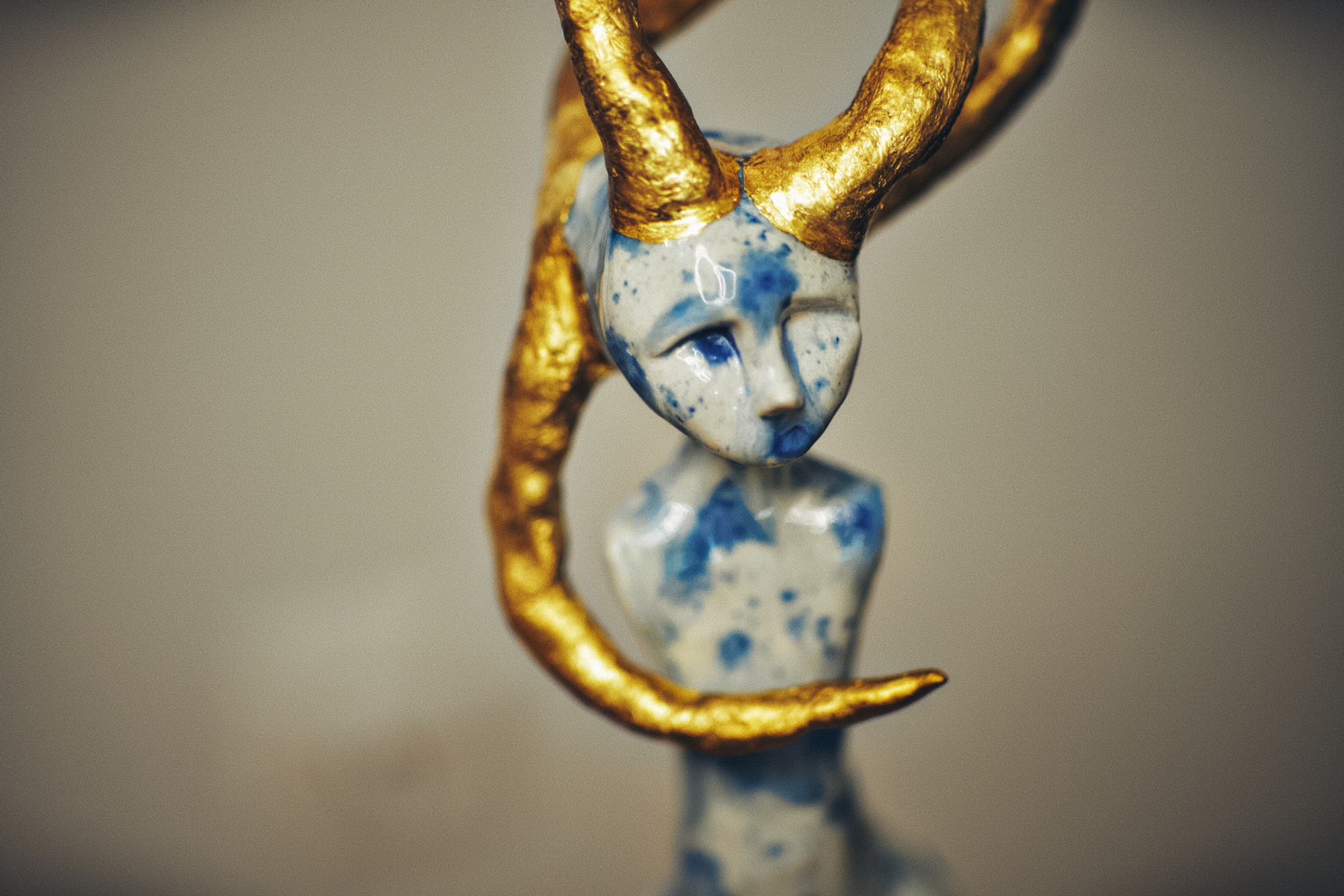 Small figurine with gold horns and blue speckled design on a neutral background